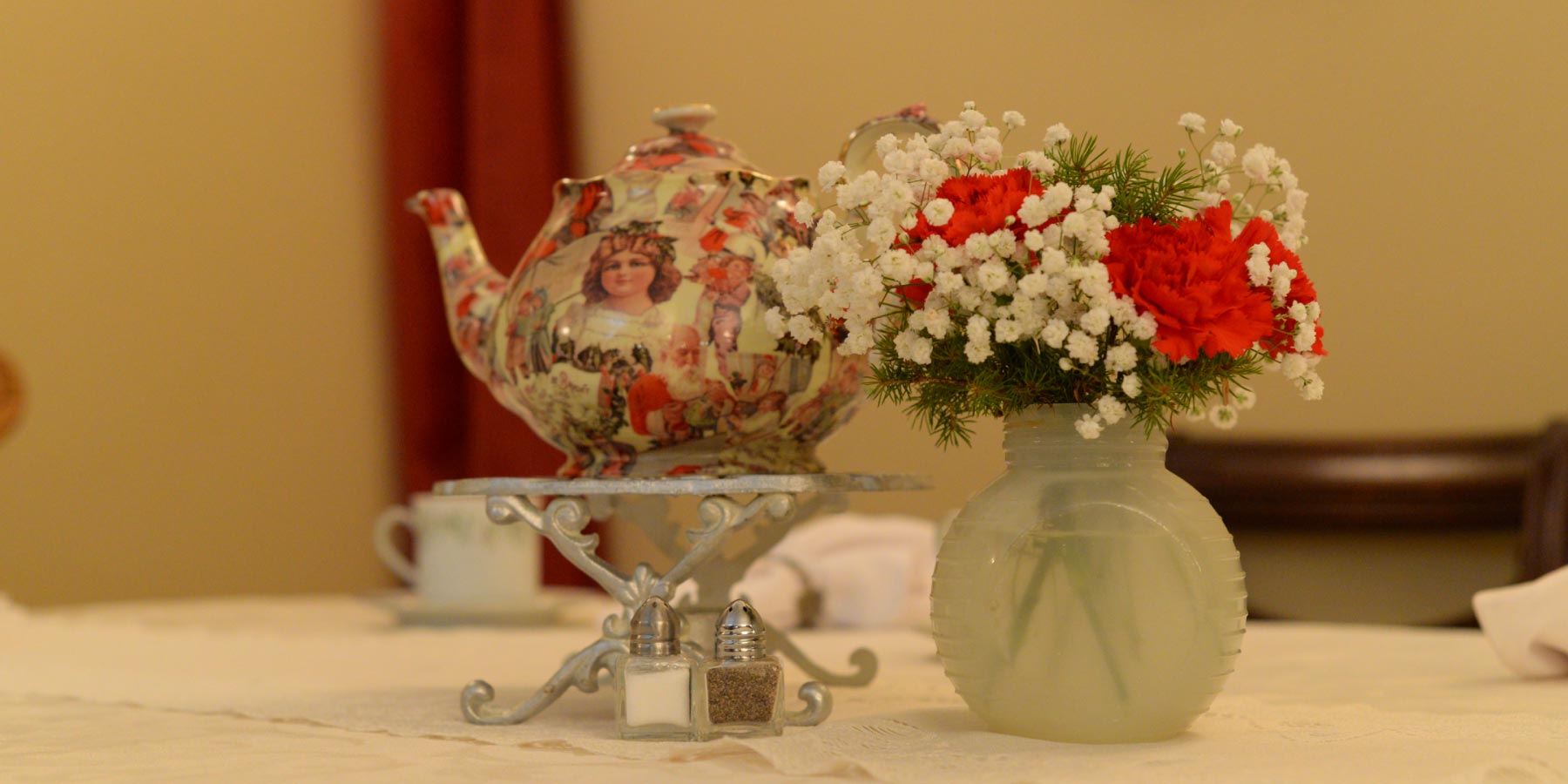A set table including a tea pot and flowers.